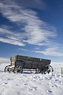 An old wooden wagon on a snow covered hillside with blue sky and clouds;Alberta canada An old wooden wagon on a snow covered hillside with blue sky and clouds;Alberta canada