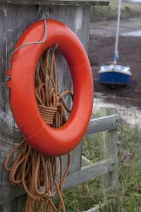 An Orange Life Preserver Ring And Rope Hanging On A Wooden Shed Wall; Northumberland, England An Orange Life Preserver Ring And Rope Hanging On A Wooden Shed Wall; Northumberland, England