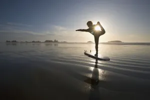 Silhouette Of Female Surfer Doing Bow Pulling Yoga Pose; Chesterman Beach Tofino Vancouver Island British Columbia Silhouette Of Female Surfer Doing Bow Pulling Yoga Pose; Chesterman Beach Tofino Vancouver Island British Columbia