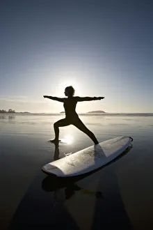 Silhouette Of Female Surfer Doing Warrior Yoga Pose; Chesterman Beach Tofino Vancouver Island British Columbia Canada Silhouette Of Female Surfer Doing Warrior Yoga Pose; Chesterman Beach Tofino Vancouver Island British Columbia Canada
