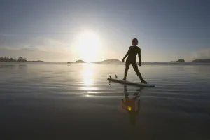 Silhouette Of Female Surfer Doing Yoga Stretches; Chesterman Beach Tofino Vancouver Island British Columbia Canada Silhouette Of Female Surfer Doing Yoga Stretches; Chesterman Beach Tofino Vancouver Island British Columbia Canada