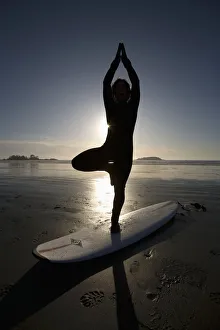 Silhouette Of Female Surfer Doing Yoga Tree Pose; Chesterman Beach Tofino Vancouver Island British Columbia Canada Silhouette Of Female Surfer Doing Yoga Tree Pose; Chesterman Beach Tofino Vancouver Island British Columbia Canada