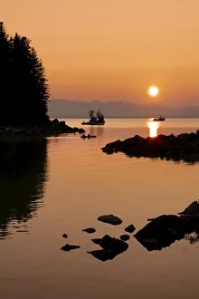 Silhouette of trawlers and a small boat along the rocky shoreline with a glowing sunset, Alaska, USA Silhouette of trawlers and a small boat along the rocky shoreline with a glowing sunset, Alaska, USA