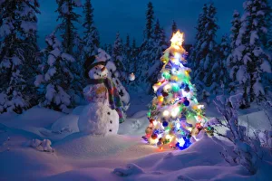 Snowman Stands In A Snowcovered Spruce Forest Next To A Decorated Christmas Tree Snowman Stands In A Snowcovered Spruce Forest Next To A Decorated Christmas Tree