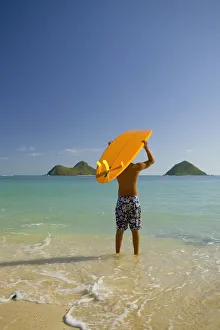 Surfer Walking Into The Water From The Beach With Board Over His Head Surfer Walking Into The Water From The Beach With Board Over His Head