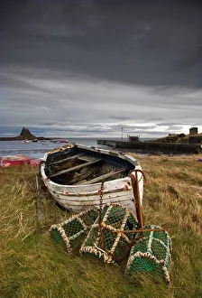 A Weathered Boat And Fishing Equipment Sitting On The Shore With Lindisfarne Castle In The Distance; Lindisfarne A Weathered Boat And Fishing Equipment Sitting On The Shore With Lindisfarne Castle In The Distance; Lindisfarne