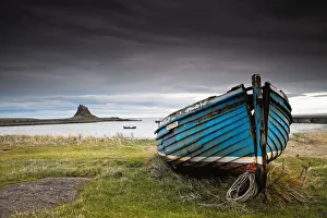 A Weathered Boat Sitting On The Shore With Lindisfarne Castle In The Distance; Lindisfarne, Northumberland, England A Weathered Boat Sitting On The Shore With Lindisfarne Castle In The Distance; Lindisfarne, Northumberland, England