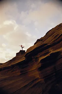 Woman Yoga At Sunrise On Rock Coastline Cliff, Side View Upward Against Clouds Woman Yoga At Sunrise On Rock Coastline Cliff, Side View Upward Against Clouds