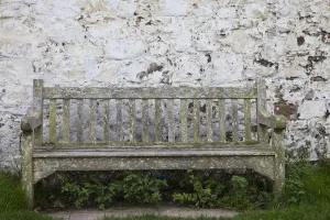 A Wooden Bench With Peeling Paint Against A White Wall; Northumberland, England A Wooden Bench With Peeling Paint Against A White Wall; Northumberland, England