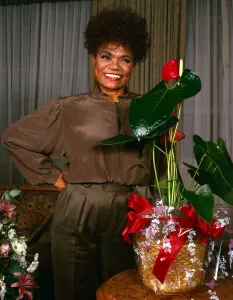 American singer and actress Eartha Kitt standing next to a plant. September 1989 American singer and actress Eartha Kitt standing next to a plant. September 1989