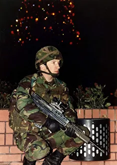 Army Soldier in camouflage uniform standing with a firearm in front of a Christmas tree Army Soldier in camouflage uniform standing with a firearm in front of a Christmas tree