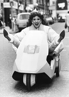 Bonnie Langford sitting in a Sinclair C5 on the road with her feet out up in a v-shape Bonnie Langford sitting in a Sinclair C5 on the road with her feet out up in a v-shape