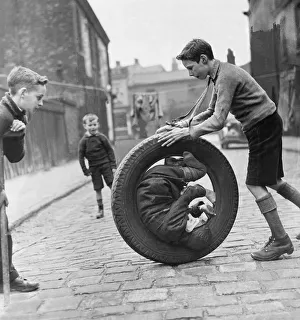 The boys are playing with a car tire, one boy is sitting inside the tire while another The boys are playing with a car tire, one boy is sitting inside the tire while another