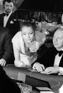 Diana Rigg in a low cut dress leans across the Black Jack table in a casino showing off Diana Rigg in a low cut dress leans across the Black Jack table in a casino showing off