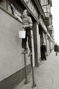 George Pettican Window Cleaner on Stilts cleaning windows on the front of his shop in George Pettican Window Cleaner on Stilts cleaning windows on the front of his shop in