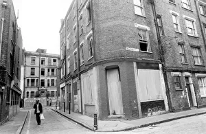 A man carrying his shopping bag as he walks past delapidated buildings with broken A man carrying his shopping bag as he walks past delapidated buildings with broken