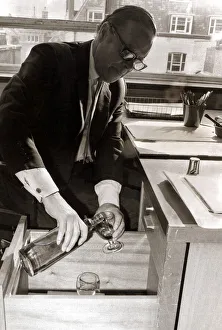A man pours himself a drink which he keeps hidden in a filing cabinet in his office at A man pours himself a drink which he keeps hidden in a filing cabinet in his office at