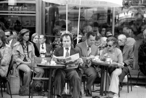 Man reading a newspaper and smoking a cigar as he sits outside in a cafe on the streets Man reading a newspaper and smoking a cigar as he sits outside in a cafe on the streets