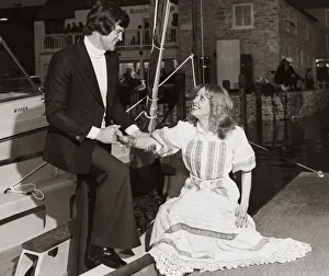 Man wearing a navy blue blazer white polo sweater and trousers helps a lady out of a boat Man wearing a navy blue blazer white polo sweater and trousers helps a lady out of a boat