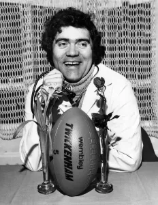 Max Boyce wearing a Doctor's cort and stethescoping the English Rose as he indicates Max Boyce wearing a Doctor's cort and stethescoping the English Rose as he indicates