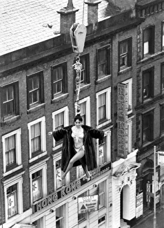 Model Linn Yamazaki demostrating the strength of her hair by hanging above rooftops on a Model Linn Yamazaki demostrating the strength of her hair by hanging above rooftops on a