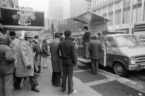 People listening to a man speaking from a platform on his van People listening to a man speaking from a platform on his van