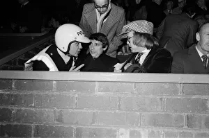 A policeman talking to Graham Taylor and Elton John, who are watching the football match A policeman talking to Graham Taylor and Elton John, who are watching the football match