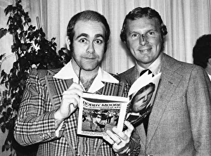 Pop star and chairman of Watford Football Club Elton John helps footballer Bobby Moore Pop star and chairman of Watford Football Club Elton John helps footballer Bobby Moore