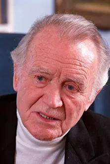 SIR JOHN MILLS IN PHOTO SHOOT AT HIS HOME SITTING IN ARMCHAIR WITH BOOKCASE AS BACKGROUND SIR JOHN MILLS IN PHOTO SHOOT AT HIS HOME SITTING IN ARMCHAIR WITH BOOKCASE AS BACKGROUND