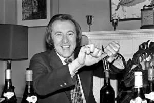 Wine: Mr. David Frost trying to open a bottle of wine at his home. March 1975 75-01338 Wine: Mr. David Frost trying to open a bottle of wine at his home. March 1975 75-01338