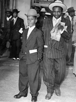 This young Jamaican boy in a striped suit and soft bowler hat has come to start a new This young Jamaican boy in a striped suit and soft bowler hat has come to start a new
