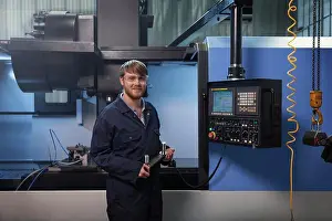 Prints of Apprentice holding a u-bolt strap in front of CNC machine November Prints: Apprentice Holding U-Bolt Strap Print