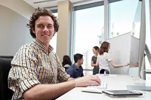 Businessman In Office Prints: Young man using computer in office looking towards camera