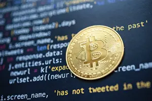 Cryptocurrency Symbol Prints: Bitcoin coin placed on top of a black screen filled with colorful programming code
