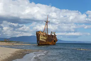 Deserted Greek Beach Prints: The bow of a rusty ship eats into the sandy beach against a blue sky and fluffy clouds