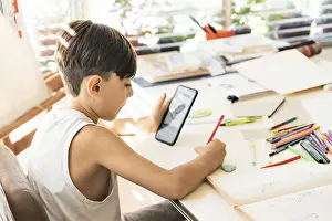 Indoor Study Space Prints: A boy is learning to draw with her smart phone