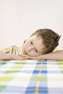Studio Shot Of A Child Prints: Boy sitting at a table, bored
