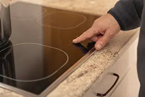 Modern Kitchen Design Prints: A close up view of a hand using the touchscreen control on a modern induction stove top