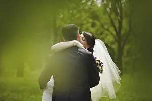 Prints of A couple embracing in a lush green setting, with the bride wearing a veil and holding a bouquet, Belarus, Minsk Belarus Prints: A Couple Embracing in Lush Green Setting Print, Belarus