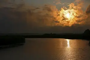 Dramatic Evening Sky Prints: Dramatic sunset behind clouds over a quiet river with golden reflection