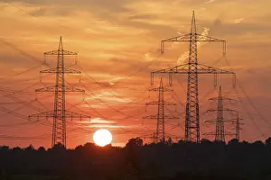 Electricity Supply Infrastructure Prints: Electric masts in front of a dramatic sunset with orange sky and clouds in the background