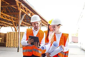 Construction Plan Blueprint Prints: Group of young architects and engineers in helmets and plan on building