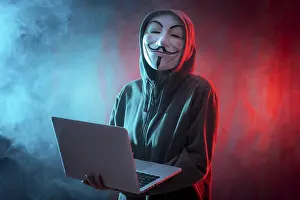 Online Technology Safety Prints: Hacker with anonymous mask with a computer and with a background of smoke and colored led