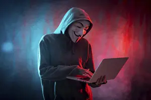 Online Technology Safety Prints: Hacker with anonymous mask with a computer and with a background of smoke and colored led