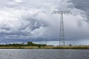 Cloudy Skies Over Germany Prints: Landscape with high power pole under dramatic waterside cloud formations