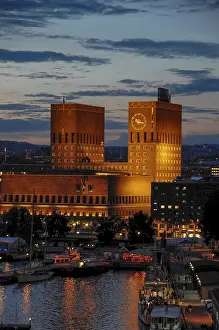 Prints of A large building with two towers and a clock, lit up at dusk with boats in the water, oslo, norway Oslo Prints: Oslo City Hall Print at Dusk, Norway