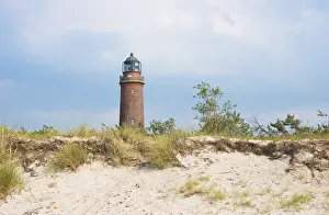 Cloudy Sky Over Dunes Prints: Lighthouse DarBer Ort behind dune with sparse vegetation