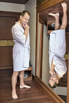 Rear View Of A Man Prints: A man in a robe meditating when looking reverse reflection in the mirror