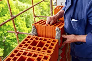 Construction Site Worker Prints: Mason, bricklayer worker is using red blocks to mount a wall next the string line to be straight