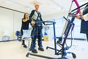 Physical Therapy Exercises Prints: Mechanical exoskeleton. Female physiotherapy medical assistant lifting disabled person with robotic skeleton